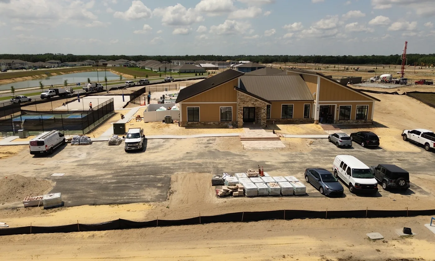Aerial drone view of a community clubhouse under construction with pickleball courts and pool