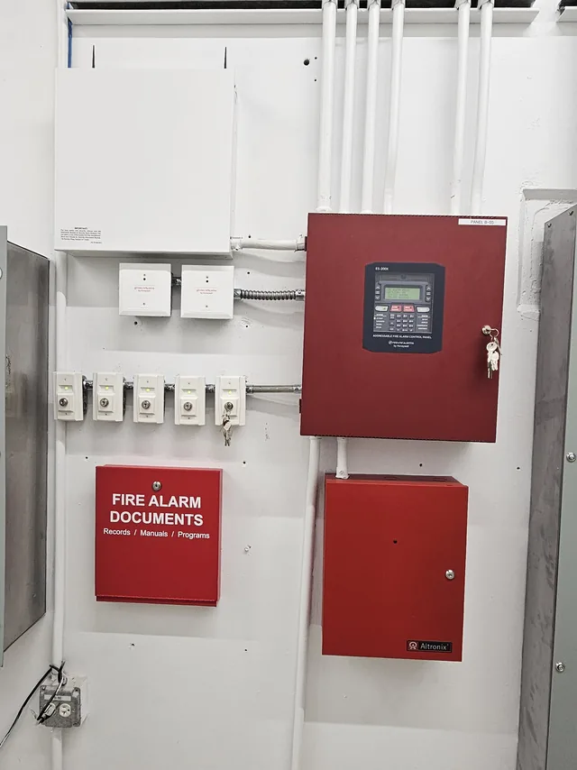 Fire alarm control panel with Altronix power supply, relay modules and document cabinet on a conduit wall