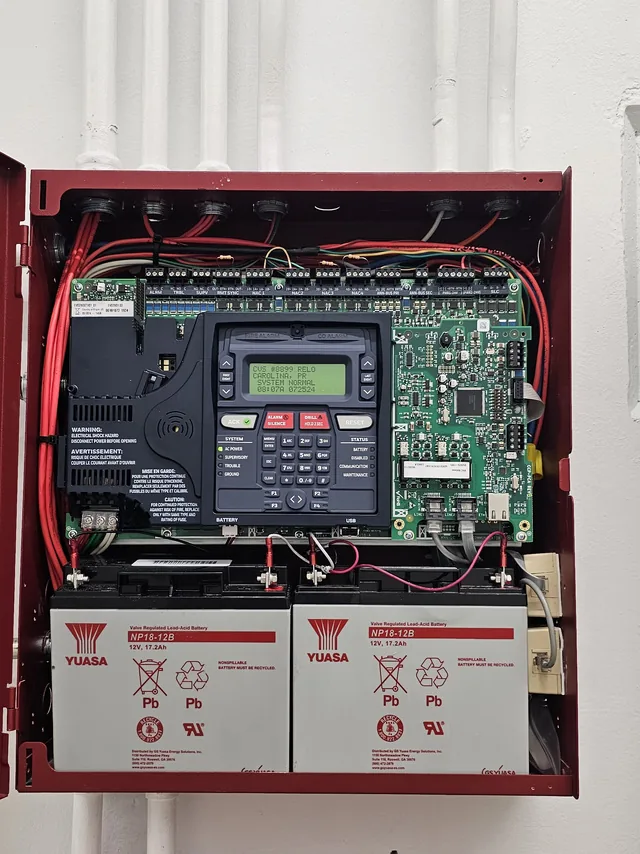 Open fire alarm control panel showing the addressable board, keypad display and sealed backup batteries