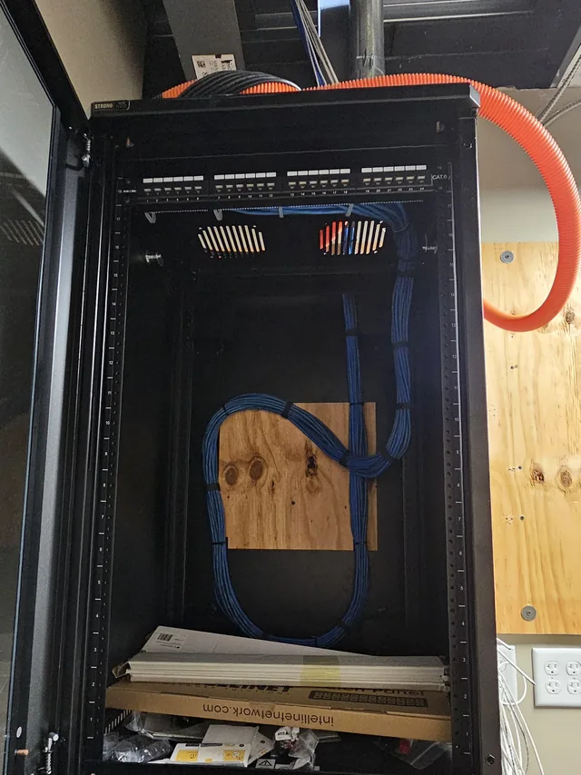 Open wall-mount network cabinet with a dressed Cat6 bundle and fiber innerduct entering from above