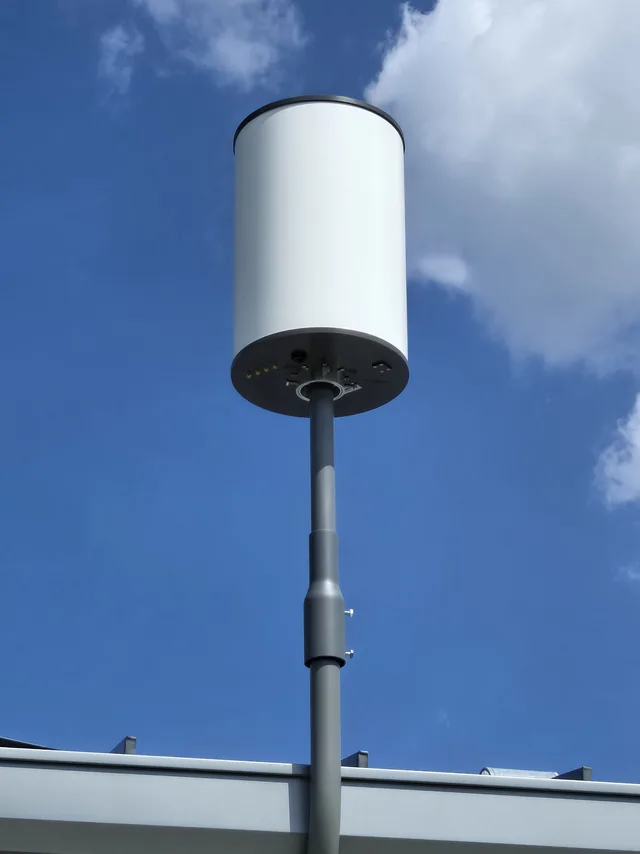 Outdoor wireless antenna on a mast above two dome security cameras under an eave