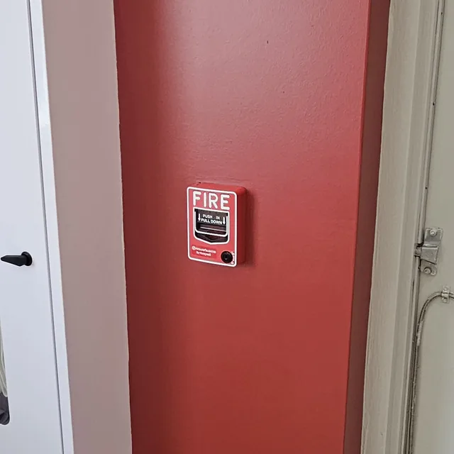 Manual fire alarm pull station installed on a red wall next to a cabinet, Winter Garden, FL