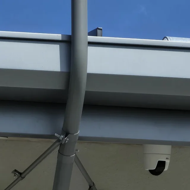 Antenna mast and a dome security camera mounted under a commercial building eave