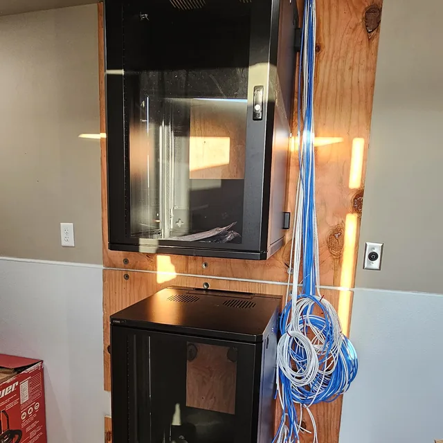 Two wall-mount network cabinets on a plywood backboard with Cat6 cable coiled for termination