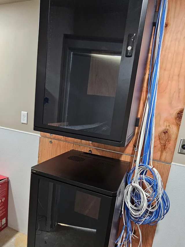 Stacked wall-mount network cabinets with Cat6 cabling roughed in on a plywood backboard